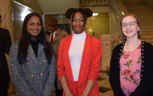 Two young Black teens and one white teen in the Maryland State House in Annapolis. One Black teen wears a black-and-white houndstooth jacket, the other a red blazer and slacks and the white girl wears a dress and cardigan.