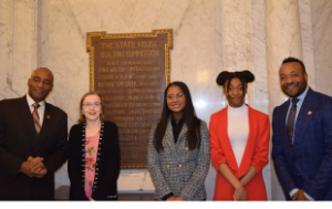 A Black middle-aged state senator, a white young teen, 2 young Black teens, and a Black delegate stand in the Maryland State House