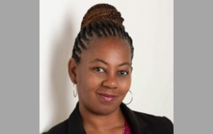 A professional headshot of Alicia McLeod, a Black woman who has her hair braided and in an updo. She wears a black blazer, a magenta shirt, and gold hoop earrings. The background is white.