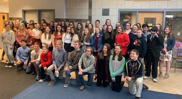 About 20-30 students pose, some kneeling in front of other standing, in a school cafeteria.