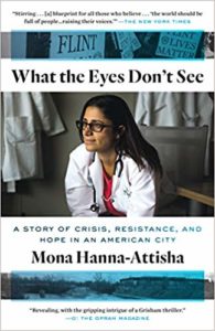 Cover ofWHAT THE EYES DON'T SEE: A STORY OF CRISIS, RESISTANCE, AND HOPE IN AN AMERICAN CITY by Mona Hanna-Attisha. The cover features Dr. Hanna-Attisha in a white doctor's coat looking left.  Above the title and protest signs about the Flint water crisis shaded in blue.