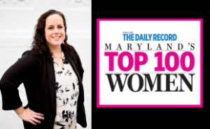 2 combined photos. On the left, a headshot of Lindsey Baker. She is a white woman with brown, curly hair past her shoulders. She wears a white button-down shirt with black flowers on it and a black blazer. Her hands are on her hips. On the right, Image that says "The Maryland Daily Record: Maryland's Top 100 Women"
