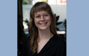 A professional headshot of Lou Williams, a white person who uses she and they pronouns. Lou has shoulder-length dirty blonde hair and glasses, smiles. They wear a dressy, short-sleeved, black blouse.