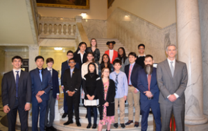 A group of 16 students, of a variety of races and genders, and two white male teachers, stand on steps at the Maryland State House in Annapolis.