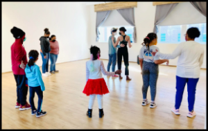 Teens and kids mostly stand in pairs as part of a dance. There is one not in a pair. Almost all of the teens and kids are Black.
