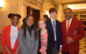 A group of 4 high schoolers and Senator Muse, Black man. The students are 2 Black girls, 1 white girl, 1 white boy.