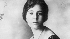 A black and white photograph of Alice Paul, a white suffragette with dark hair tied into a low bun. She is wearing a dark top with a light collar.