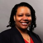 Christian Pulley, a middle-aged Black woman, smiles. She wears a black blazer and red top. The background is gray.