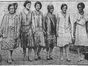 A 1930 stylized image of 7 Black women in skirts and dresses a little lower than the knee, in various shades and low heels. The third from the right wears a hat. The image looks to be candid and some women are smiling slightly. Estelle Hall is third from the right and August Chessell is third from the left.