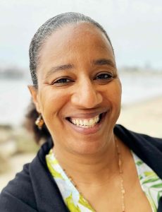 Myriam J.A. Chancy, a Black woman who wears a printed white shirt, black sweater, and hair in a ponytail.